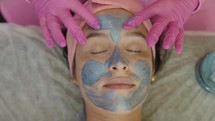 Close-up shot of a woman enjoying facial treatment with clay mask at beauty shop. Cosmetology and spa
