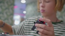 A 12-year-old boy in a striped t-shirt assembles a construction toy in a cafe, with a slight blur on his face, focusing on his engaged hands.