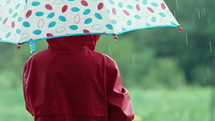 Unrecognizable child boy with umbrella under rain. Kid in red raincoat enjoying.