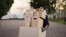 Delivery man in uniform, cap and gloves carrying many heavy cardboard boxes parcels outdoor.