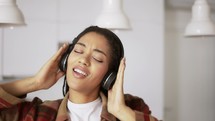 Portrait of the young woman wearing headphones listening to the music at home, slow motion.