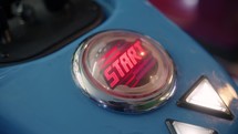 Close-up of a blinking start button on a motorcycle game in an arcade. A girl's hand presses it