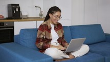 Positive girl with dreadlocks is laughing and smiling with laptop on knees.