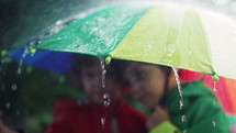 Happy preschool children brothers boys under umbrella during downpour. Smiling kids in raincoats enjoys autumn weather. Colorful parasol, raindrops, carefree childhood. High quality 4k footage