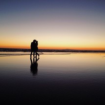 A couple embrace on an ocean beach at dusk.