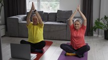 Active mature couple performing stretching exercise by online workout lessons using laptop.
