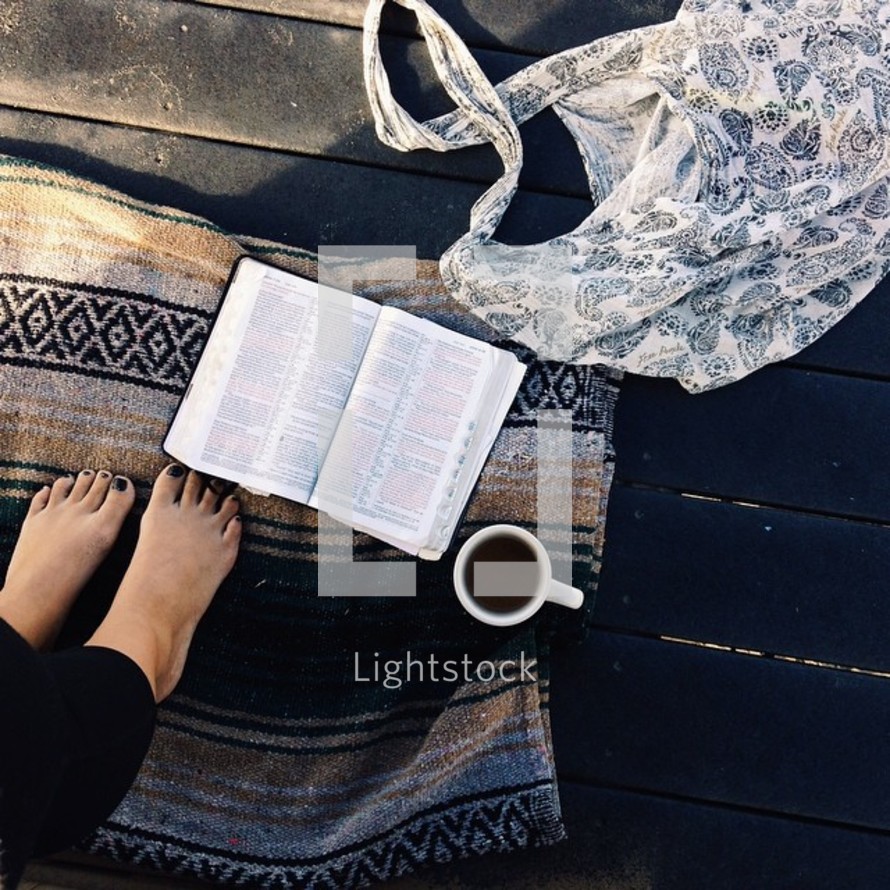 woman with bare feet standing on a blanket and a cup of coffee and an open BIble 