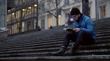 a man sitting on steps in a city reading a Bible in winter 