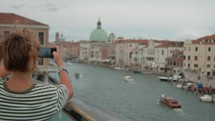 A teenager in a striped shirt captures a panoramic view of the Grand canal with the distinct San Simeone Piccolo church in the background