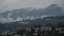 Apartment buildings in the foreground with rolling hills and a mountain range engulfed in mist in the background