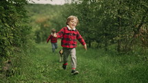 Happy kids running together with beagle puppy in green garden. Smiling brothers, stylish boys having fun with dog, playing outdoors. Friendship, family, twins, childhood concept