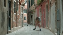 A teenager performs the bottle flip challenge on a street in Venice, Italy. As the bottle lands upright, he triumphantly raises his hands and a pigeon flies in the background