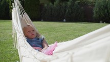 A young girl lounges in a white hammock, lost in thought, with a lush garden in the background