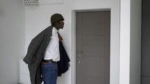 Black man in front home door putting on trendy coat, leaving house, slow motion.