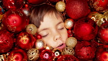 Toddler boy sweet sleeping, child face, red Christmas tree balls.