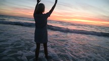 woman with raised hands walking into the ocean 