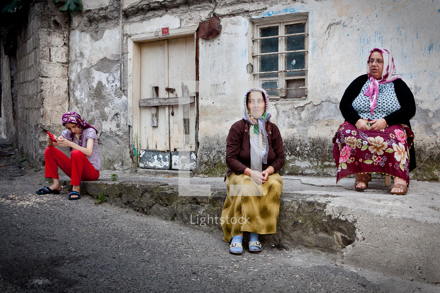 women wearing scarves on their heads sitting on a street curb 