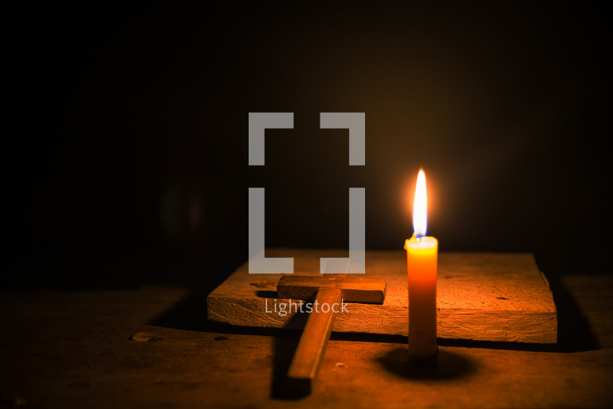 Wood cross on a dark background lit up by a candle