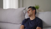 Pensive man sitting home in modern living room closeup. Portrait of attractive serious guy thinking on life problem pondering decisions alone. Worried  male feeling loneliness resting at couch
