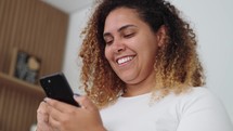 Happy Black woman holding cell phone using smartphone device at home. 
