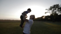 Happy father and son. A loving father playing with his happy young boy, holding and hugging him affectionately in the evening sunset or sunrise sunlight in cinematic slow motion.