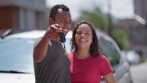 Young hispanic couple kissing each other holding key of new car at street
