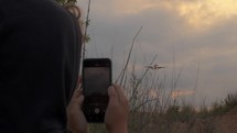 Unrecognizable teenager in a sweatshirt records a video on his mobile phone as the plane comes in for landing with its landing gear extended