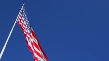 American flag against a blue sky blowing on a flag pole 