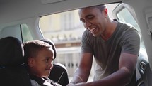 safe ride, loving father puts his little cute male child in back seat in baby car seat and fasten safety belts before driving
