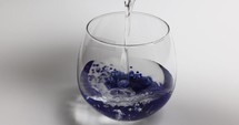 Pouring Clean Water Into A Glass With Purple Jelly Beads. close up