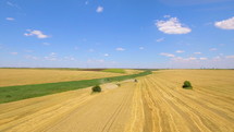 Aerial drone shot of a combine harvester working in a wheat field in summer day with blue sky and clouds.