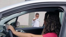 Happy schoolboy with a backpack waving goodbye to mother before going for lessons in elementary school. Loving mom saying goodbye to her son before the school while sitting in the car. 
