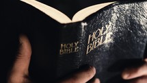 Man reading and closing The Holy Bible in dark and moody professional lighting