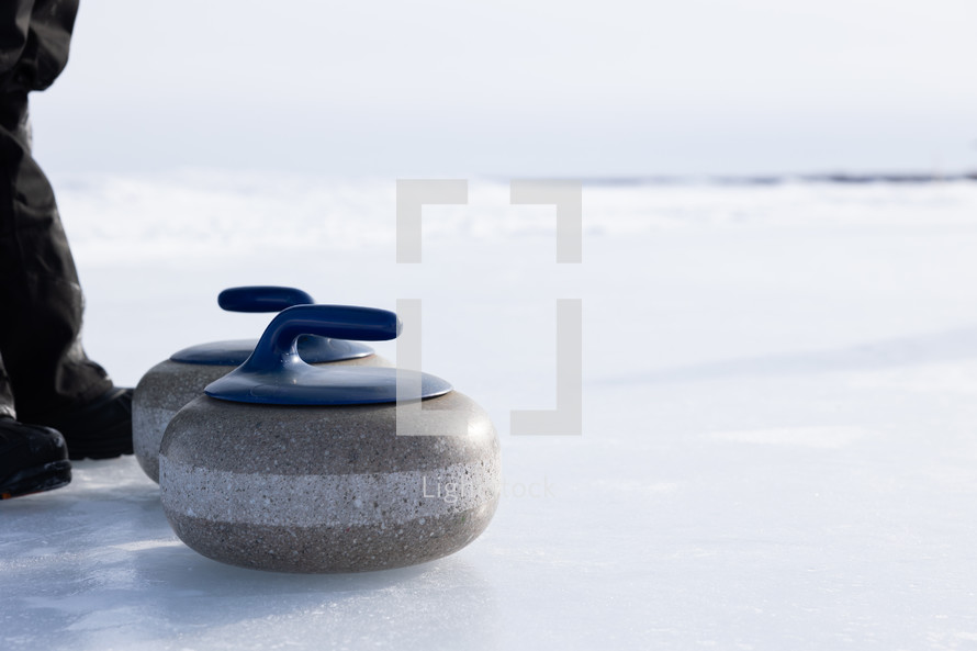 Two blue curling rocks on a frozen lake