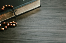 Wood rosary on a closed  bible on a dark wood background with copy space