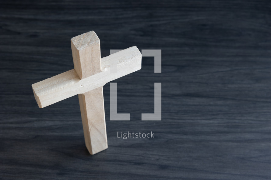 Small wood cross standing on a dark wood table from above