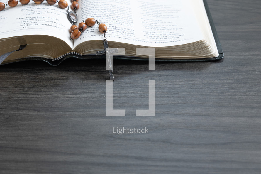 Wood rosary on an open bible on a dark wood background with copy space