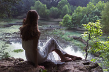 a woman sitting on a rock near a river 