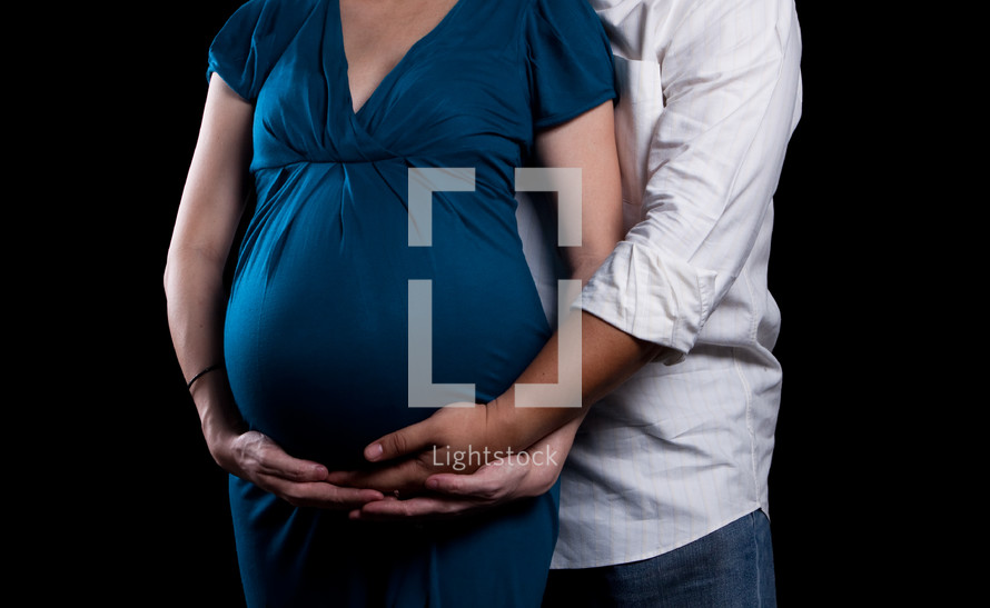 torso of an expecting woman and man holding her belly 