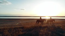  View of women riding horses along the river in golden light sunset or sunrise. Stallion walking in desert by the water. Slow motion.
