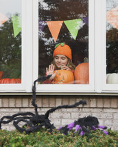 A girl with a jack-o-lantern looking out a window 