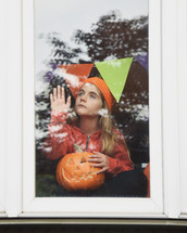 a girl with a jack-o-lantern looking out a window 