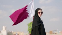 Portrait of Young beautiful girl in traditional Abaya dress with of Qatari flag waving. 
