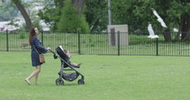 Woman pushing stroller through park birds flying by - slow motion