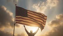 Man waving american flag against blue and orange sky with white clouds