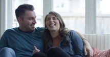 Happy young couple watching tv - full belly laugh