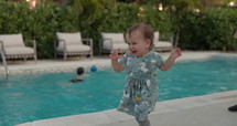 Toddler girl running around swimming pool in summer with clothes on