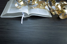 gold streamers and open bible on a dark wood background