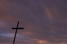 Cross against sunset sky of purple, pink and grey clouds