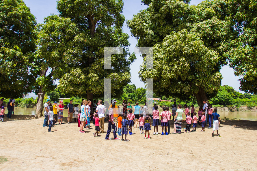 people gathered outdoors on sand under trees 